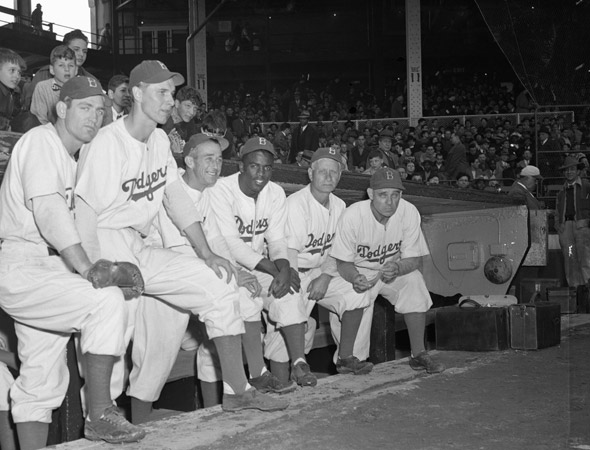 "Members of the Brooklyn Dodgers and their new coach pose in front of their dugout before an exhibition game with the New York Yankees. The team has a new manager and new Negro star player from Montreal, Jackie Robinson."